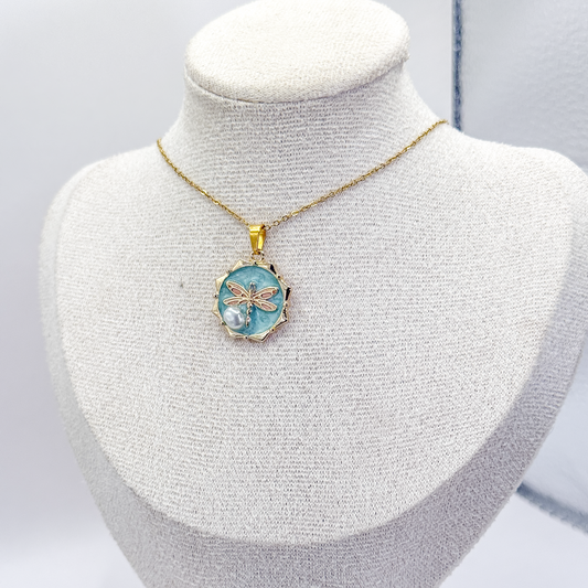 Collar dorado con dije circular azul esmaltado, libélula rosa y detalle aperlado